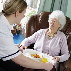 An attendant handing a tray of food to a resident in a recliner chair