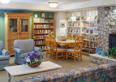 Library room with fireplace, bookshelves full of books, dining table, floral sofa and blue chairs.